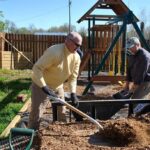 Tim Borman shovels mulch into a wheelbarrow for Bob Hansen to distribute around the playset.